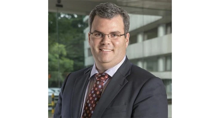 A man smiles with a gray suit and a red tie.