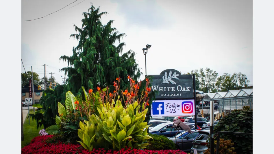 Trees, flowers and signage in front of a garden center asking people to follow on Facebook and Instagram.