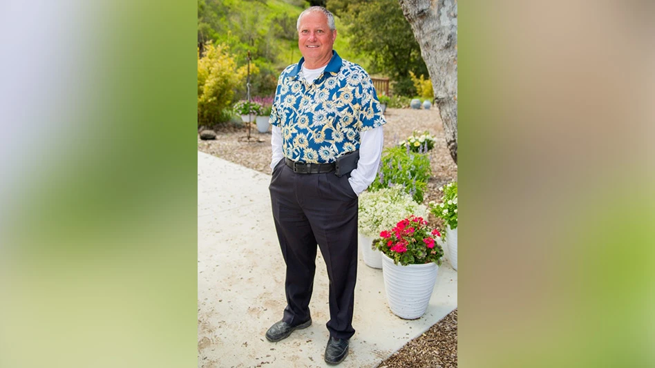 A man poses smiling in front of a garden.