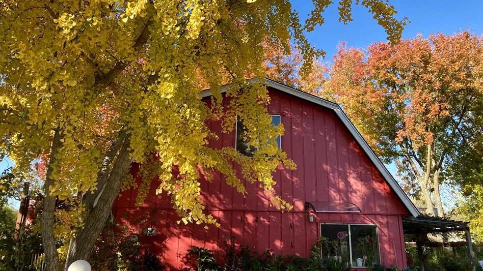 A red barn with orange and yellow trees around it.