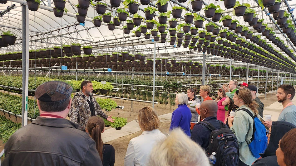 A group of people standing inside a greenhouse while on a nursery production tour.